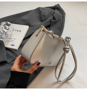 Detail of metallic silver handbag featuring irregular wave handle and knot strap detail