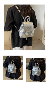 Detail of silver metallic mini backpack featuring a decorative bow and drawstring closure