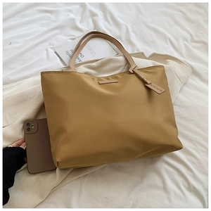 Detail of khaki oxford tote bag with leather handles and size reference next to a phone