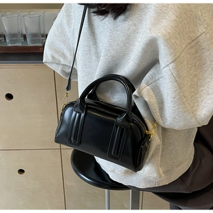 Chic black Boston bag with gold hardware worn by a model in a warm lifestyle setting