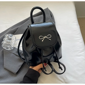Close-up of black patent leather mini backpack with silver bow buckle and drawstring