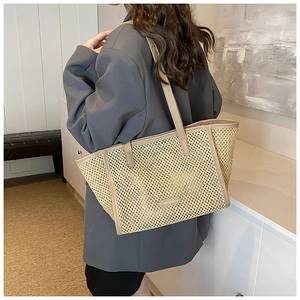 Détail d'un sac cabas en paille tissée avec bordure en cuir kaki et plaque logo HOCOMU