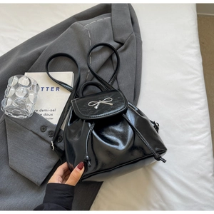 Close-up of black glossy bucket backpack with silver bow buckle on office aesthetic background