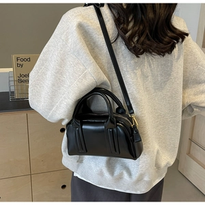 Detailed view of a small black Boston bag with gold hardware on a crossbody strap