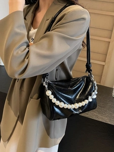 Schwarze glänzende Achseltasche mit Perlenkette und Herzanhänger am Modell getragen