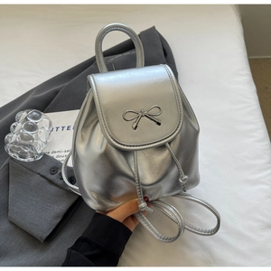 Detail of silver metallic mini backpack featuring a bow buckle and drawstring closure