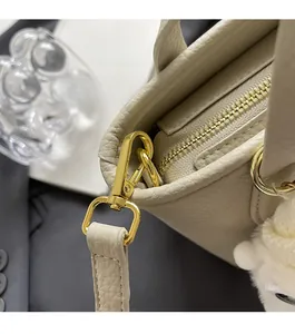 Close-up of premium beige leather handbag featuring shiny gold hardware and plush ball charm