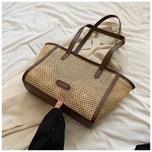 Détail du cabas en paille tissée avec bords en cuir marron sur un tissu blanc