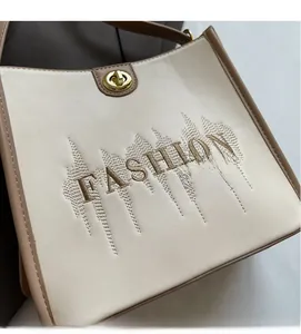 Detail of cream tote bag with brown trim, fashion embroidery and golden metal twist lock
