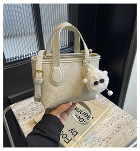 Close-up of cream pebble leather bucket bag with a funny monster plush charm