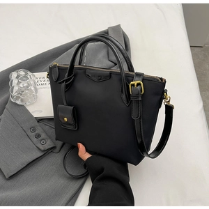 Detail of black nylon tote bag with gold hardware and removable strap on grey suit