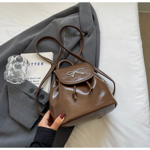 Detailed view of a brown faux leather mini backpack featuring a silver bow and drawstring