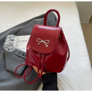 Detail of red shiny mini backpack with silver bow decoration and drawstring closure