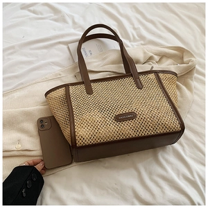 Détail d'un grand sac en paille tressée avec garniture en cuir brun et logo ovale