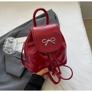 Detail of red glossy leather mini backpack with silver bow and top handle on grey fabric