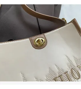Close-up of golden swivel lock and brown brand embroidery on a beige leather tote bag