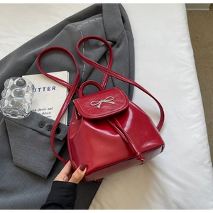 Detail of red glossy leather mini backpack featuring silver metal bow and drawstring closure