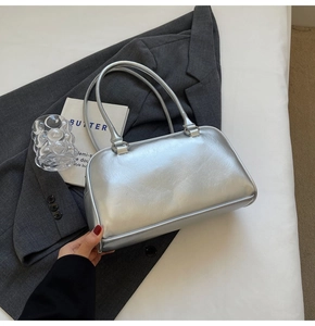 Vue détaillée du sac à main argenté métallisé sur un blazer gris avec livre d'art