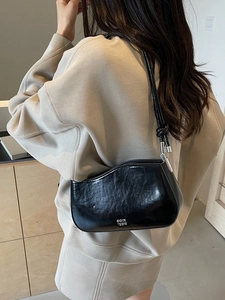 Minimalist black patent leather shoulder bag with knot detail shown on a model