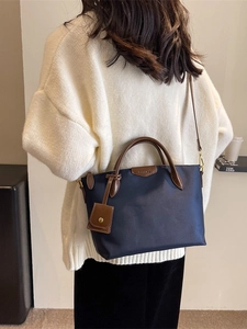 Navy blue nylon tote bag with leather handles shown on model in a cozy setting