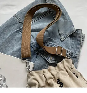 Gros plan du sac seau en toile beige avec broderie dollar et bandoulière tressée