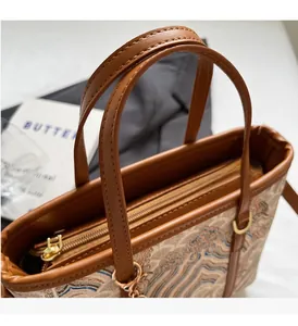 Close-up of the brown leather handles and golden metal zipper on a textured tote bag