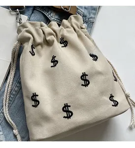 Détail du sac seau en toile blanc cassé avec broderie de signe dollar noir et cordon
