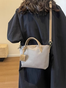 Minimalist grey tote bag with brown handles carried by a model in a long coat