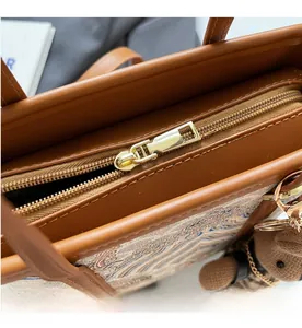 Detail of smooth gold zipper and cute knit bear charm on brown leather bucket bag