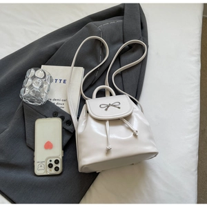 Close-up of cream white mini backpack featuring silver bow buckle and drawstring closure