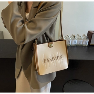 Detail view of beige tote bag with brown trim and Fashion embroidery worn by a model
