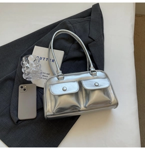 Vue de dessus d'un sac à main argenté métallisé posé sur un blazer gris avec accessoires