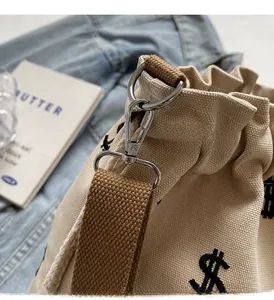 Détail du sac seau en toile beige avec fermoir en métal argenté et bandoulière marron