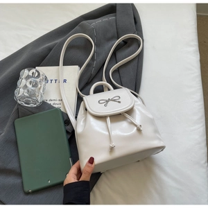 White mini backpack with silver bow decoration placed on a grey suit and white bedding