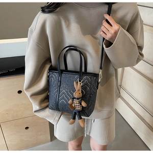 Detail of black leather bucket bag with gold wavy embroidery and a cute rabbit charm