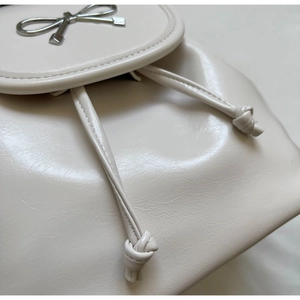 Close-up of cream leather backpack featuring silver metal bow and drawstring detail