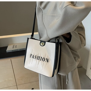 Detail of cream white tote bag with FASHION print, metal buckle and black shoulder strap