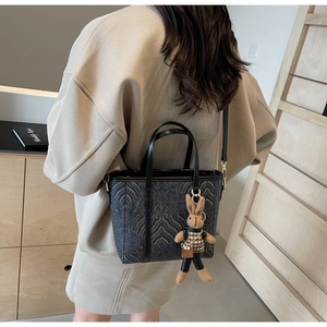 Detail of black textured bucket bag with decorative bunny pendant and crossbody strap