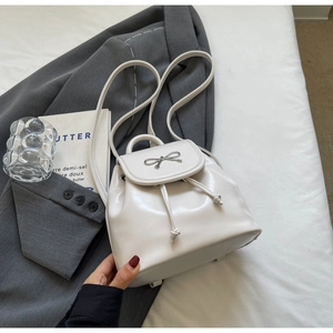 Close-up of white mini backpack with metal bow detail and drawstring on grey blazer