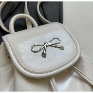 Close-up of cream white glossy leather backpack with silver metal bow detail and texture