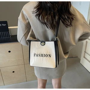 Detail of cream crossbody bag with black trim, fashion text and golden twist lock