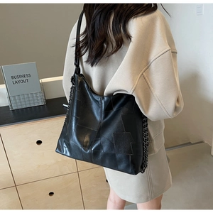 Detail of black patchwork leather tote bag with metal chain strap worn by a model
