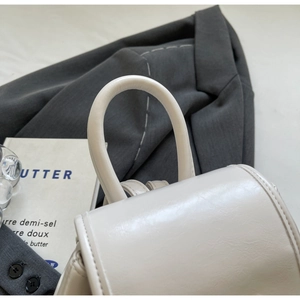 Detail shot of the cream white leather mini backpack with curved handle and minimal flap design