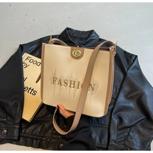 Detail of beige tote bag featuring gold FASHION embroidery and metallic twist lock closure