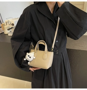 Detailed side view of beige pebble leather tote bag with plush monster charm and top handles
