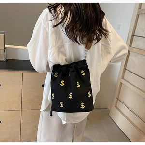 Détail d'un sac seau noir à cordon avec broderie du signe dollar jaune sur le tissu