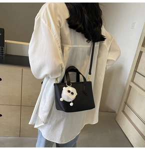 Detail of black lychee grain bucket bag with dual handles and plush eye charm accessory