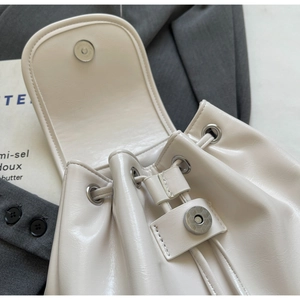Detail of cream faux leather backpack with drawstring closure and silver magnetic buckle