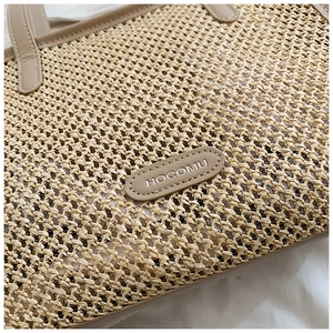Gros plan du sac cabas en paille avec écusson et poignée en cuir marron