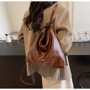 Close-up of a vintage brown leather tote bag with geometric stitching and metal chain strap